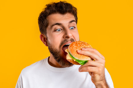 Closeup Portrait Of Hungry Guy Eating Burger On Yellow Background