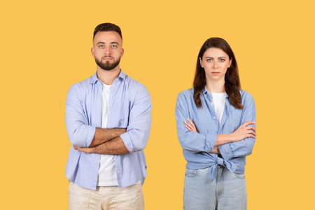 Two young adults in casual attire, standing with arms crossed on yellow backgroundの写真素材