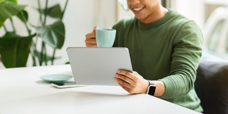 Cropped black guy chilling at cafe, drinking coffee, using tablet