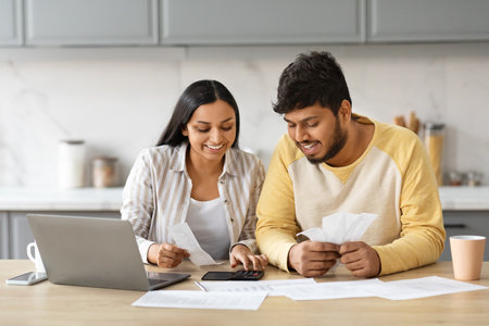 Smiling indian couple holding papers, calculating domestic bills, kitchen interiorの写真素材
