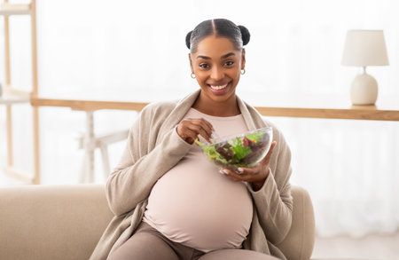 Happy young black lady expectant eating fresh vegetable salad