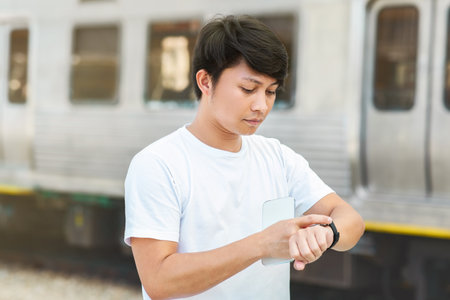 Asian guy looking at watch standing on city streetの写真素材