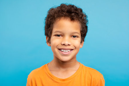 Cheerful curly-haired boy in orange t-shirt, blue background