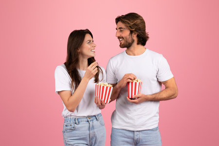 Happy young caucasian man and woman in white t-shirts eat popcorn at movie nightの写真素材
