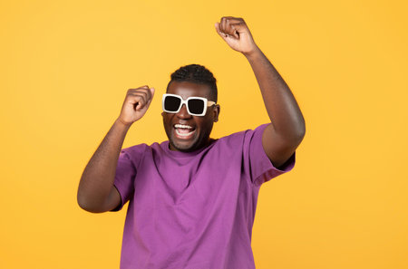 african guy in trendy sunglasses celebrating and dancing, yellow backgroundの写真素材