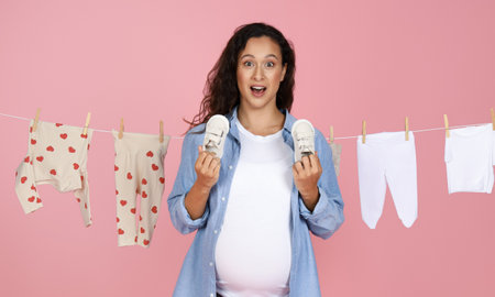 Excited mom-to-be with baby shoes on pink backgroundの写真素材