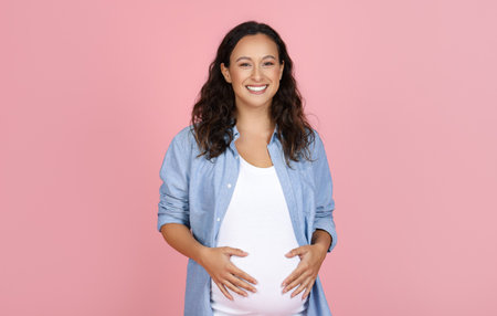 Happy young pregnant woman posing on pink backgroundの写真素材