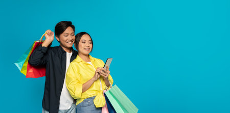 Smiling couple with shopping bags, the woman engaged with her smartphoneの写真素材