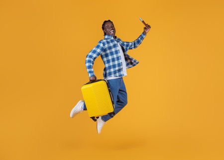 Portrait Of Young Happy Black Man Jumping With Suitcase And Passportの写真素材