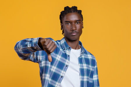 Dissatisfied young black man showing thumb down gesture at cameraの写真素材