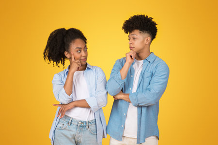 Thoughtful young African American woman and man with hands on chin, looking at each otherの写真素材