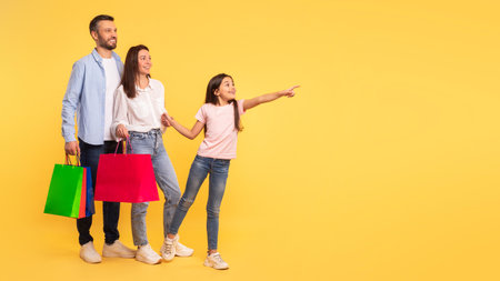 Happy Parents And Daughter Holding Shopper Bags Pointing Aside, Studioの写真素材