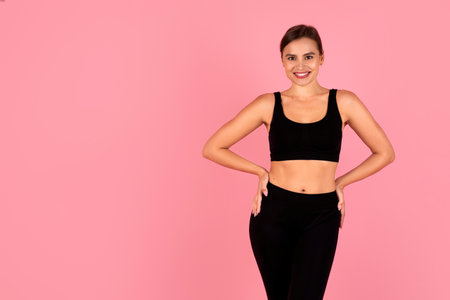 Smiling woman in sportswear with hands on hips posing on pink backgroundの写真素材