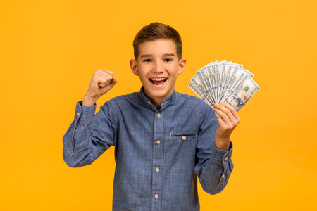 Joyful teen boy triumphantly raising fist while holding dollar cashの写真素材