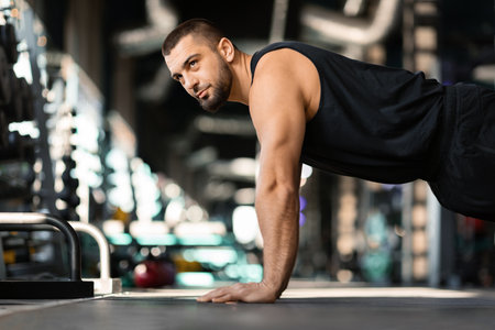 Motivated young male doing floor push-ups exercises while training in gymの写真素材