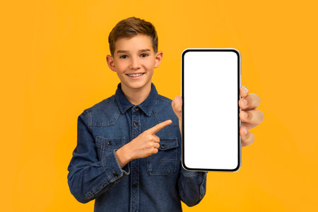Cool offer. Smiling teen boy pointing at big blank smartphone in handの写真素材
