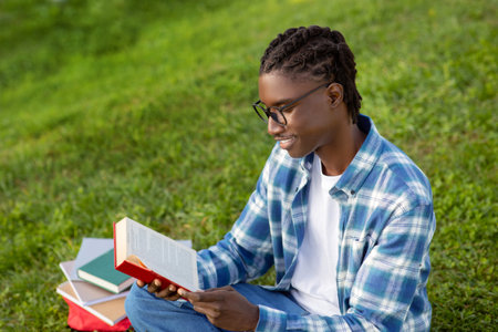 black man wearing glasses happily reads book relaxing in parkの写真素材