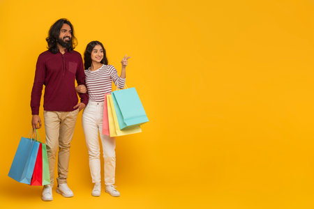 Cheerful millennial indian couple shopping together on yellowの写真素材