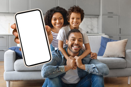 Cheerful african american family of three showing blank smartphone with white screenの写真素材