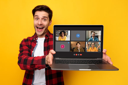 A jovial man in a red plaid shirt excitedly presents a laptop screen with a smiling group