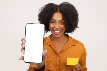 Delighted African American woman with curly hair showing a smartphone with a blank screenの写真素材