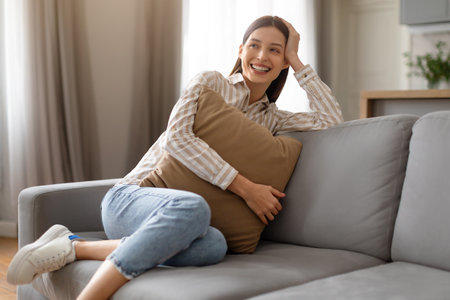 Joyful young woman relaxing with pillow on the sofa at home and smilingの写真素材