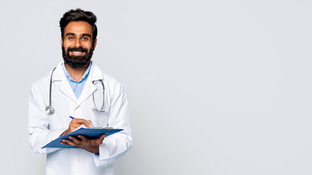 Smiling male doctor writing on clipboard, grey background, free spaceの写真素材