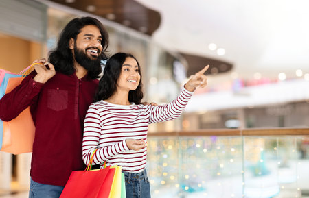 Affectionate young eastern couple standing in shopping mall with purchasesの写真素材