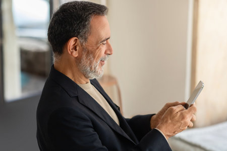 Profile view of a cheerful senior man in a smart casual outfit using a smartphoneの写真素材