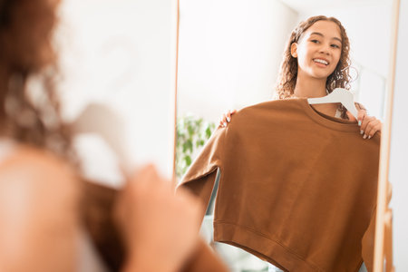 Happy teen girl trying on sweatshirt looking in mirror indoorsの写真素材