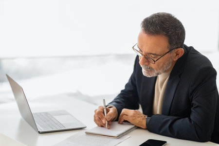 A thoughtful, mature businessman in a smart suit takes notes with a pen in a notebookの写真素材