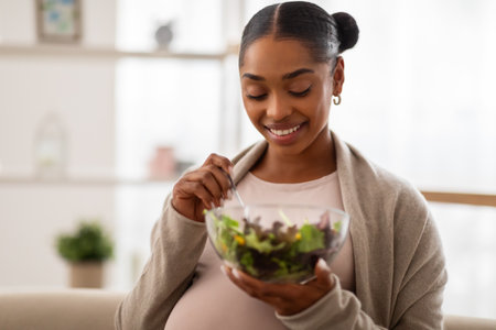 Portrait of happy young pregnant woman eating salad at homeの写真素材