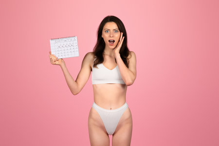 Shocked young woman in white underwear holding a calendar with a surprised expressionの写真素材
