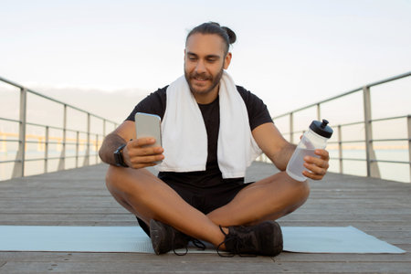 Sporty guy checking his smartphone after workout takes break outdoor