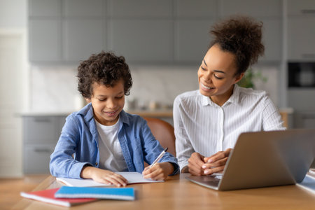 Black mother helps her son with homework at kitchen table