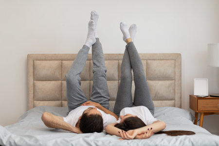Relaxed young couple lying in bed with legs raisedの写真素材