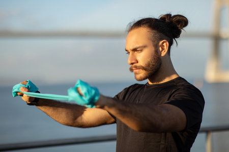athlete guy in sportswear practices workout with resistance band outdoors