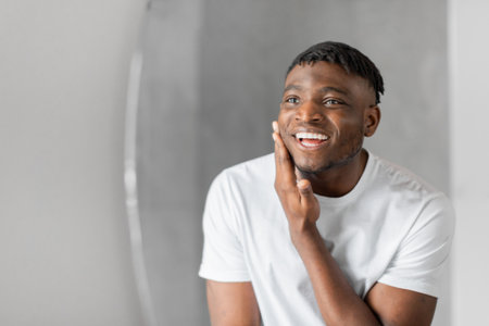 black guy stands in bathroom looking at mirror touching face
