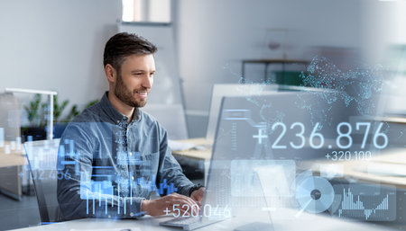 Smiling male professional working on a laptop in a bright office, with virtual financial charts