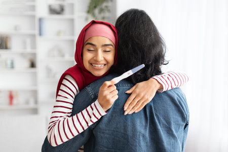 Happy Excited Young Muslim Woman Holding Positive Pregnancy Test And Hugging Husbandの写真素材