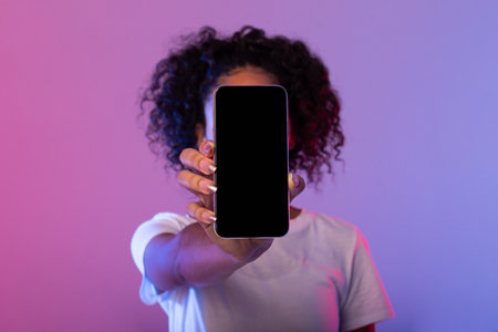 Lady showing smartphone with blank screen, covering face against neon backgroundの写真素材