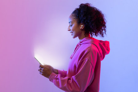 Content black lady in hoodie using phone, neon light glow