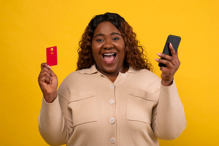 Happy young black woman using cell phone and credit card