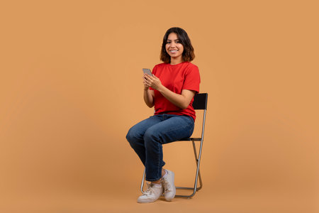 Positive arab woman sitting on chair with smartphone in handsの写真素材