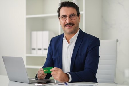 Cheerful businessman in a dark blue suit holding a credit card ready to make an online payment