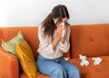 Sick Young Woman Blowing Nose In Paper Tissues At Homeの写真素材