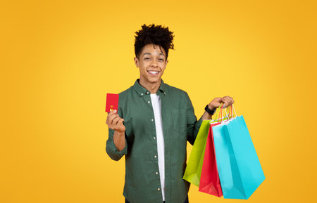 Positive african american guy showing credit card and purchases