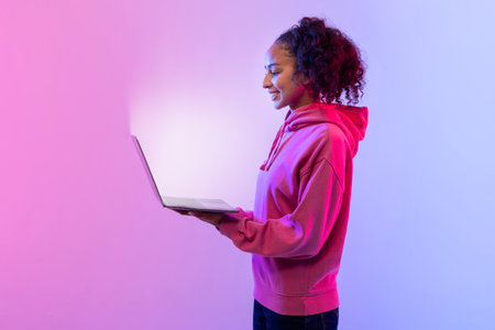 Smiling young woman with laptop glowing against pink and blue background