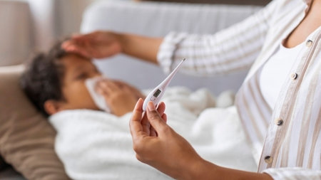 Black mother touching sons forehead and checking his temperature with digital thermometer