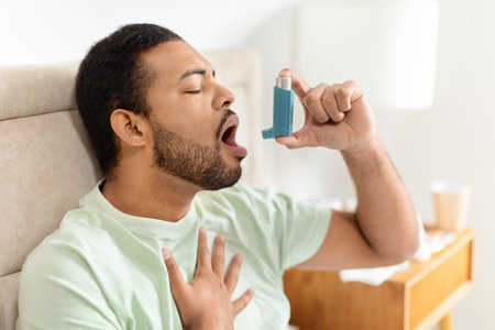 Handsome black man sitting alone at home, using asthma pumpの写真素材